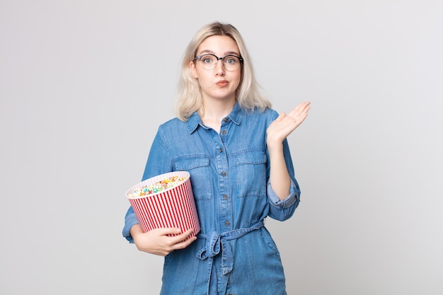 Junge hübsche Albino-Frau, die sich verwirrt und verwirrt fühlt und mit einem Popcorn-Eimer zweifelt