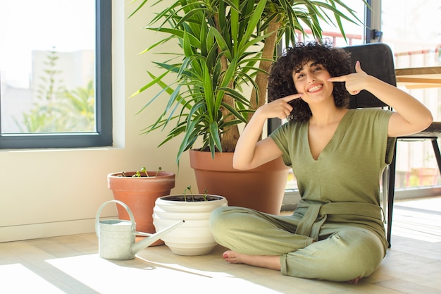 Junge hübsche arabische Frau zu Hause, mit einer Gießkanne und Pflanzen