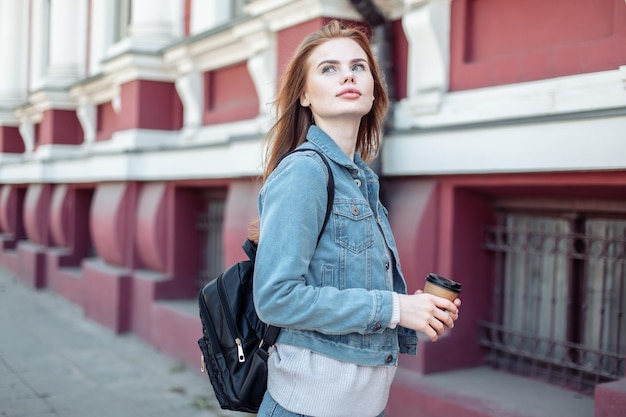 Junge, hübsche, attraktive Frau in Jeansjacke mit einer Kaffeetasse in der Stadt