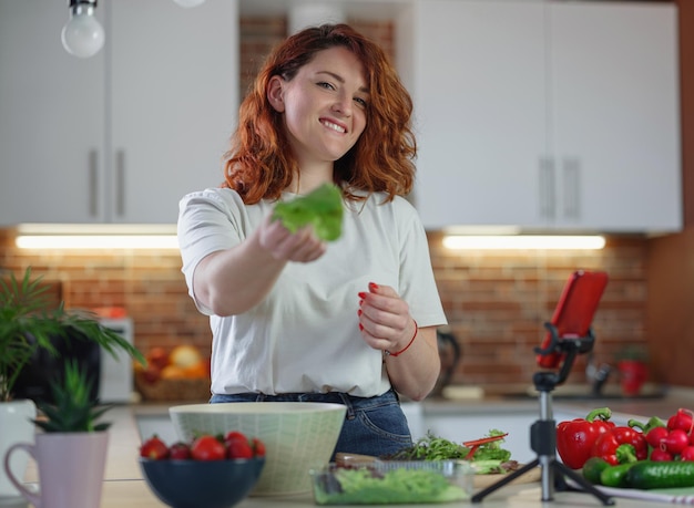 Junge hübsche Bloggerin dreht mit einer Smartphone-Kamera ein Video eines Salatrezepts