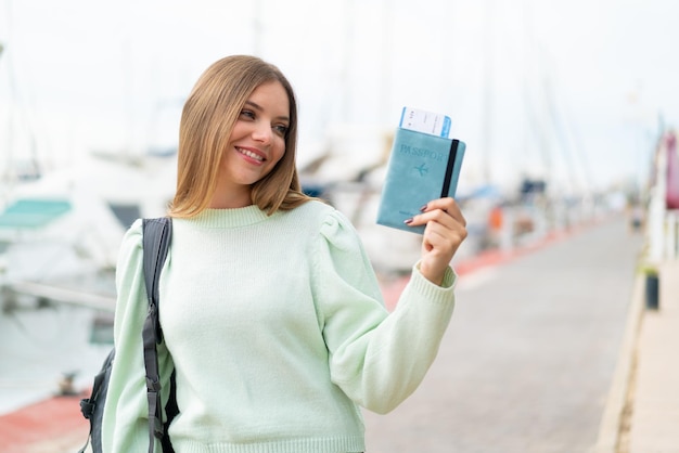 Foto junge hübsche blonde frau, die draußen einen pass mit glücklichem ausdruck hält