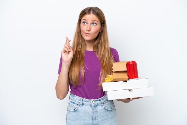 Junge hübsche blonde Frau hält Fast Food isoliert auf weißem Hintergrund mit gekreuzten Daumen und wünscht das Beste