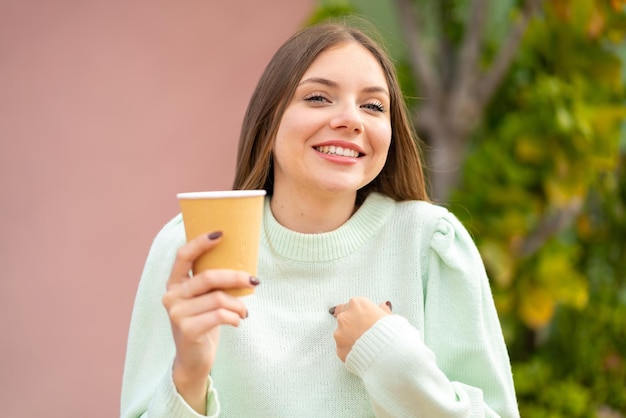 Junge hübsche blonde Frau mit einem Kaffee zum Mitnehmen im Freien mit überraschendem Gesichtsausdruck