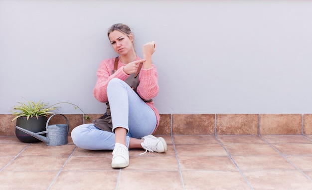 Junge hübsche blonde Gärtnerin sitzt auf dem Boden mit einem Kopierraum zur Seite