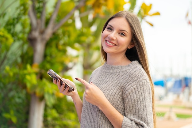 Junge hübsche Blondine, die draußen Handy benutzt und es zeigt