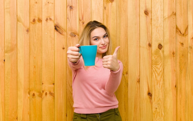 Junge hübsche Blondine mit einer Kaffeetasse gegen hölzerne Wand