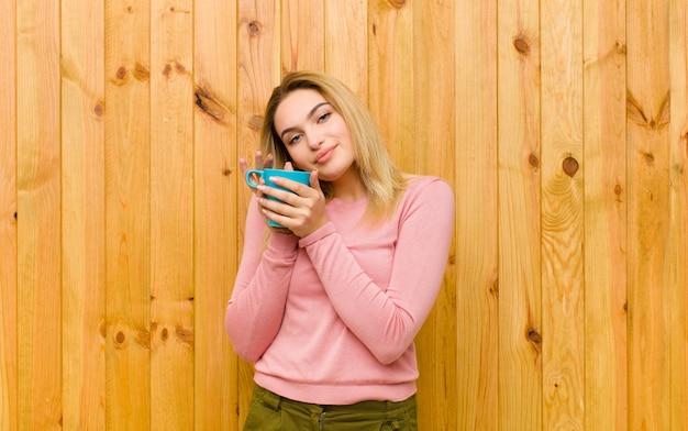 Junge hübsche Blondine mit einer Kaffeetasse gegen hölzerne Wand