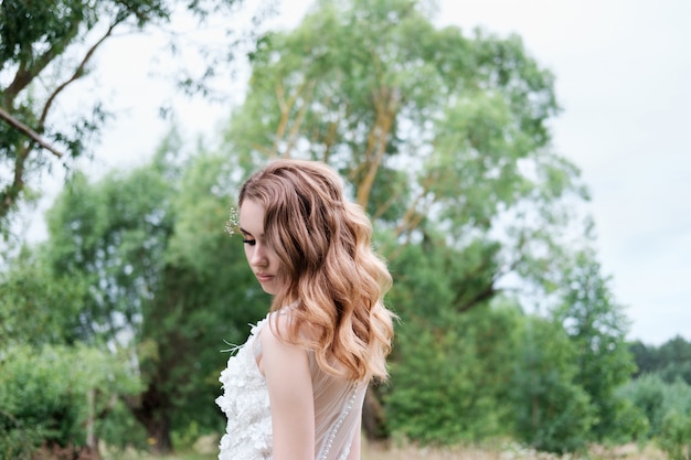 Junge hübsche Braut im weißen Hochzeitskleid im Freien, Make-up und Frisur