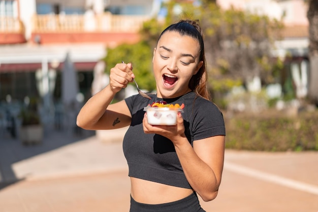 Junge hübsche brünette Frau hält draußen eine Schale Obst in der Hand