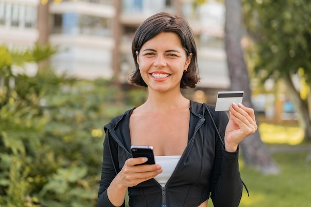 Junge hübsche bulgarische Frau im Freien, die mit dem Handy und einer Kreditkarte einkauft