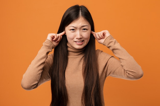 Junge hübsche chinesische Frau, die Ohren mit seinen Händen bedeckt.