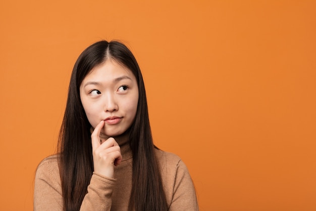 Junge hübsche chinesische Frau, die seitwärts mit zweifelhaftem und skeptischem Ausdruck schaut.