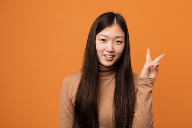 Junge hübsche chinesische Frau froh und sorglos, ein Friedenssymbol mit den Fingern zeigend.
