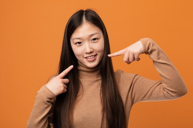 Junge hübsche chinesische Frau lächelt und zeigt mit den Fingern auf den Mund.