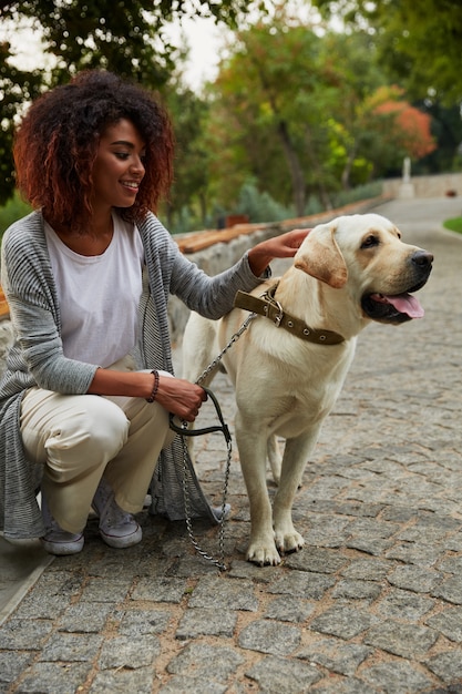 Junge hübsche Dame, die mit freundlichem Hund im Park sitzt