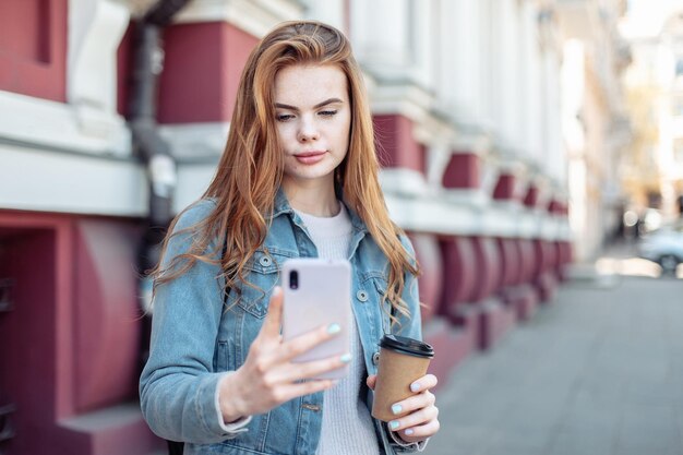 Junge hübsche Frau benutzt Smartphone und hält eine Tasse Kaffee in der Stadt