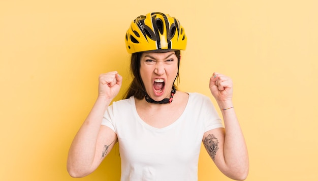 Junge hübsche Frau, die aggressiv mit einem wütenden Ausdruck Fahrradhelm-Konzept schreit