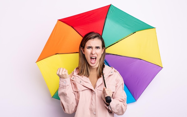 Junge hübsche Frau, die aggressiv mit einem wütenden Ausdruck schreit. Regenschirm-Konzept