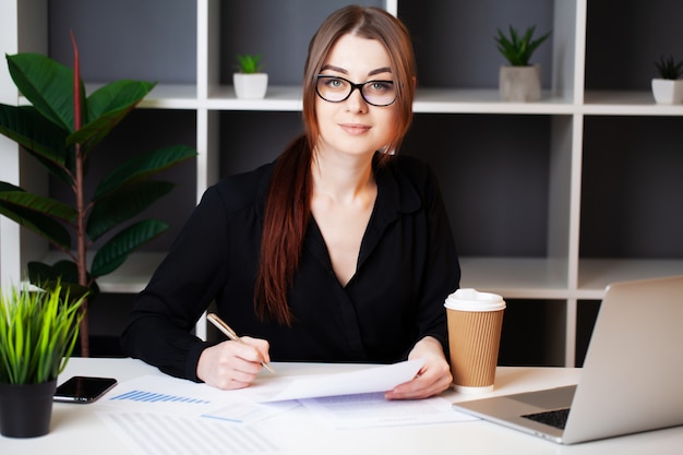 Junge hübsche Frau, die am Computer im Büro arbeitet und Dokumente füllt