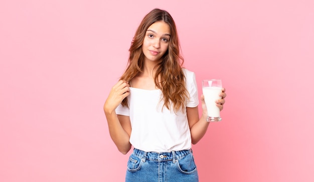 Junge hübsche Frau, die arrogant, erfolgreich, positiv und stolz aussieht und ein Glas Milch hält