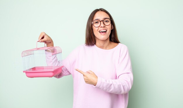 junge hübsche frau, die aufgeregt und überrascht aussieht und auf die seite zeigt. Haustierkäfig-Konzept