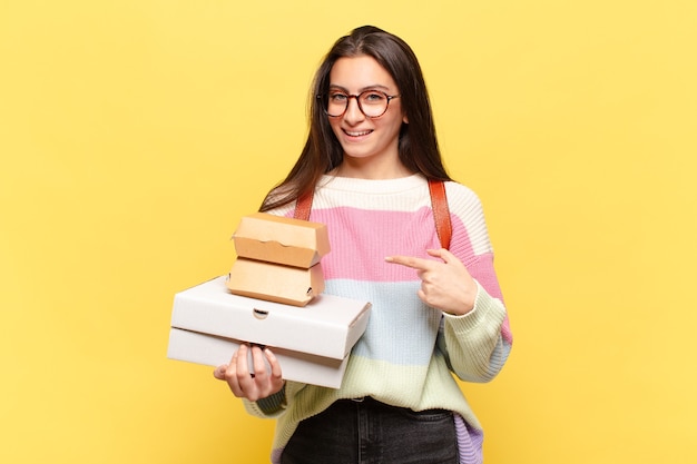 Junge hübsche Frau, die aufgeregt und überrascht schaut und zur Seite und nach oben zeigt, um Raum zu kopieren. Nehmen Sie ein gutes Fast-Food-Konzept