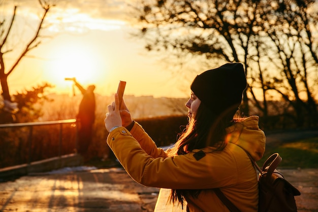 Junge hübsche Frau, die bei Sonnenuntergang ein Foto auf ihrem Telefon macht. Lebensstil