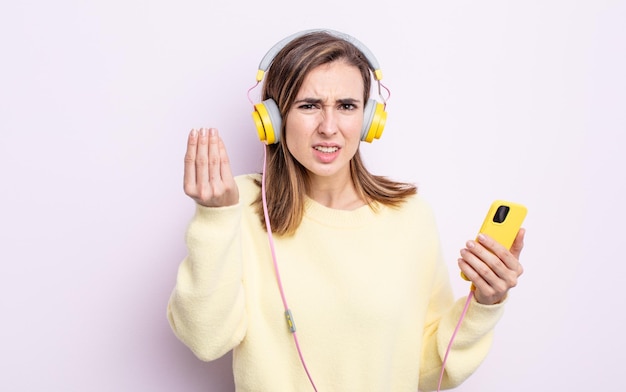 Junge hübsche frau, die capice oder geldgeste macht, die ihnen sagt, kopfhörer und telefonkonzept zu bezahlen