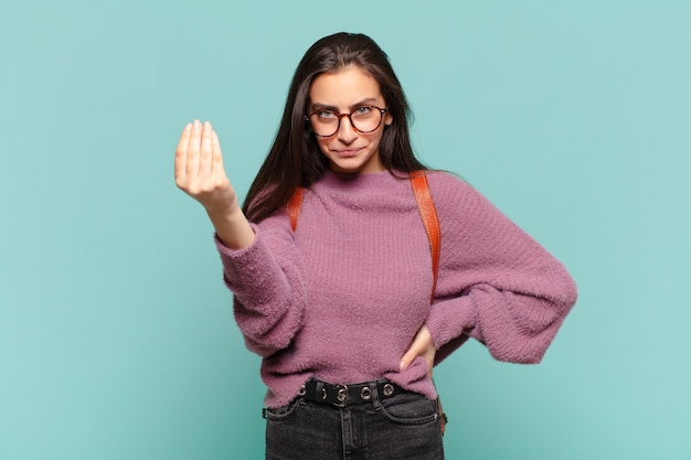 Junge hübsche Frau, die Capice oder Geldgeste macht und Ihnen sagt, dass Sie Ihre Schulden bezahlen sollen!. Studentenkonzept