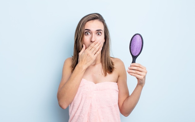 Junge hübsche Frau, die den Mund mit den Händen mit einem schockierten Haarbürstenkonzept bedeckt