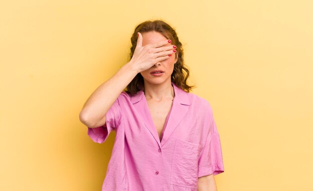 Junge hübsche Frau, die die Augen mit einer Hand bedeckt, fühlt sich ängstlich oder ängstlich, wundert sich oder wartet blind auf eine Überraschung