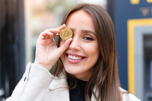 Junge hübsche Frau, die draußen ein Bitcoin hält