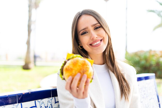 Junge hübsche Frau, die draußen einen Burger mit glücklichem Ausdruck hält