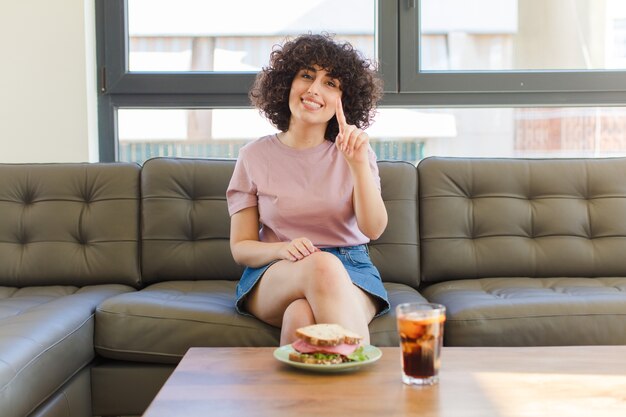 Junge hübsche Frau, die ein Sandwich auf einem Sofa zu Hause sitzt