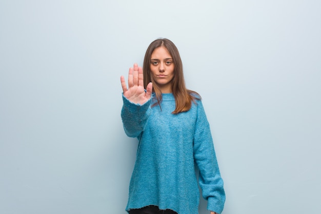 Junge hübsche Frau, die eine blaue Strickjacke einsetzt Hand in Front trägt