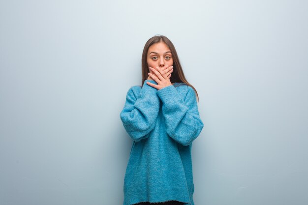 Junge hübsche Frau, die eine blaue Strickjacke überrascht und entsetzt trägt