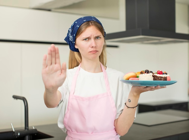 Foto junge hübsche frau, die ernst aussieht und offene handfläche zeigt und stopp-geste macht. konzept für selbstgebackene kuchen