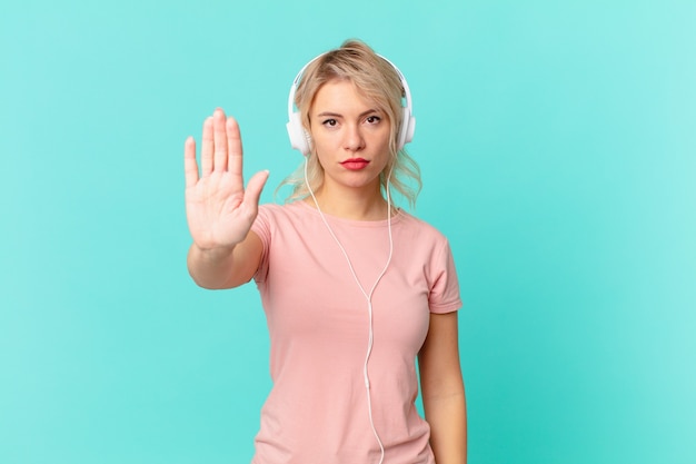 Junge hübsche Frau, die ernsthafte offene Handfläche zeigt, die Stoppgeste macht. Musik hören