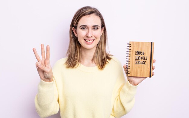 Junge hübsche Frau, die freundlich lächelt und aussieht und Nummer drei zeigt. Recycling-Konzept