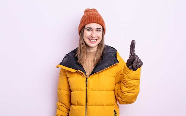 Junge hübsche Frau, die freundlich lächelt und aussieht und Nummer eins zeigt. Winterkonzept