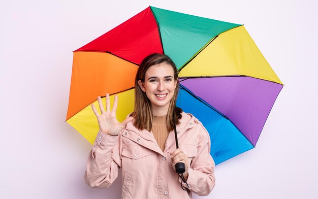 Junge hübsche Frau, die freundlich lächelt und aussieht und Nummer fünf zeigt. Regenschirmkonzept