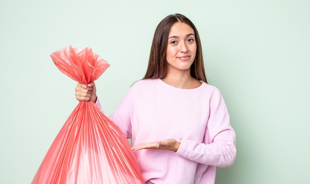 Junge hübsche Frau, die fröhlich lächelt, sich glücklich fühlt und ein Konzept zeigt. Trash-Konzept