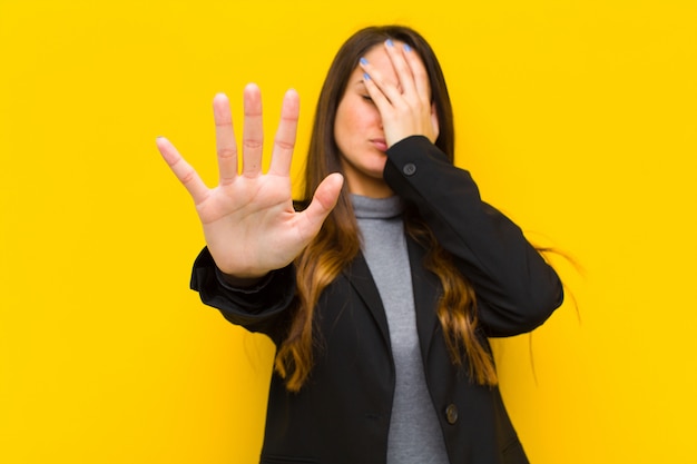 Junge hübsche Frau, die Gesicht mit Hand bedeckt und andere Hand vorne setzt, die Fotos oder Bilderjob oder Geschäftskonzept ablehnt