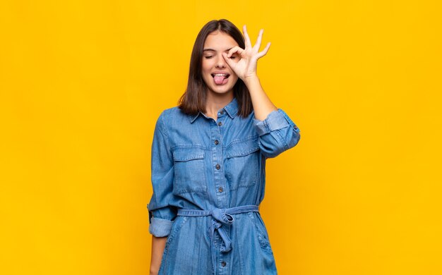 Junge hübsche Frau, die glücklich mit lustigem Gesicht lächelt, scherzt und durch Guckloch schaut