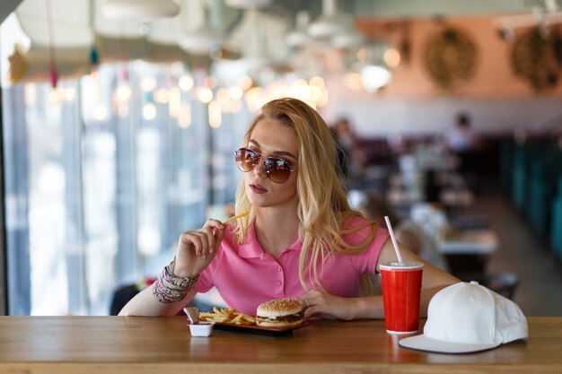 Junge hübsche Frau, die im Café ausruht und Burger isst