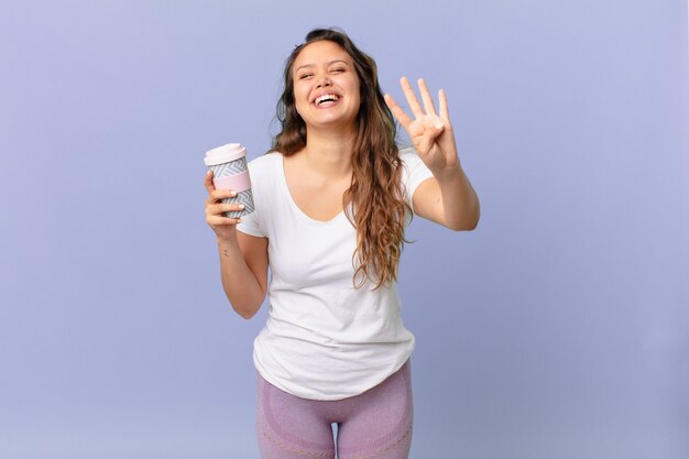 Junge hübsche Frau, die lächelt und freundlich aussieht, Nummer vier zeigt und einen Kaffee hält?