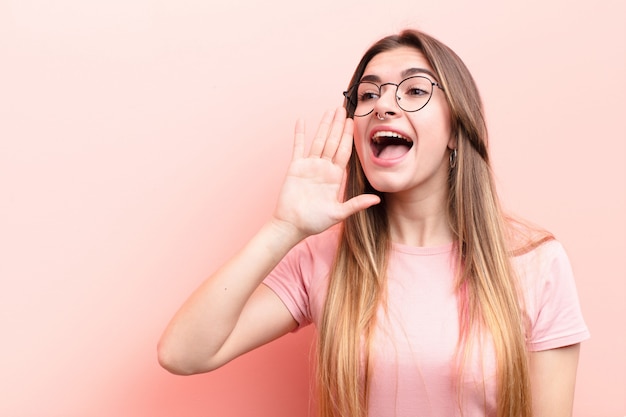 Junge hübsche Frau, die laut und wütend schreit, um Platz auf der Seite zu kopieren, mit Hand neben Mund gegen rosa Wand