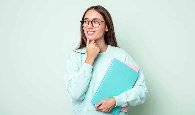 Junge hübsche Frau, die mit einem glücklichen, selbstbewussten Ausdruck mit der Hand am Kinn lächelt. Universitätsstudent