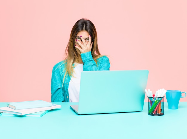 Junge hübsche Frau, die mit einem Laptop sich langweilt, frustriert und schläfrig fühlt nach einer lästigen, stumpfen und langweiligen Aufgabe, Gesicht mit der Hand halten arbeitet