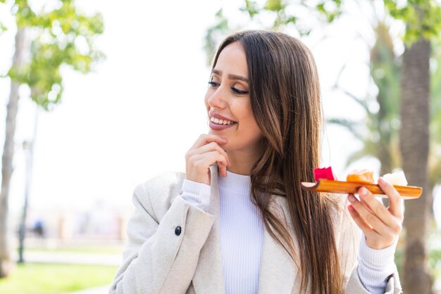 Junge hübsche frau, die sashimi im freien hält, denkt an eine idee und schaut zur seite